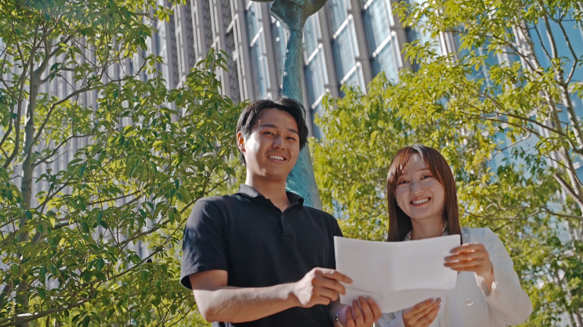 社屋前で資料を見ながら話す 福岡 と先輩社員